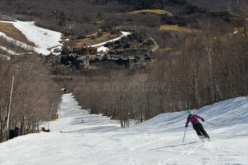 Free rider seen from behind making a turn in Stowe Mountain resort in Vermont during Spring in mid-April warm sunny day. Stowe village view at the valley
