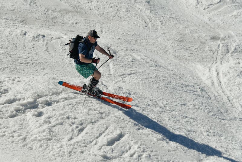 Free rider seen from side angle, wearing swim shorts and making a turn in Stowe Mountain resort in Vermont during Spring in mid-April warm sunny day