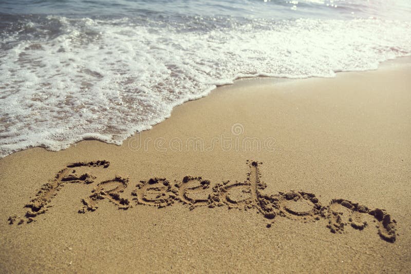 Word freedom handwritten in golden sand on the beach next to the waterline