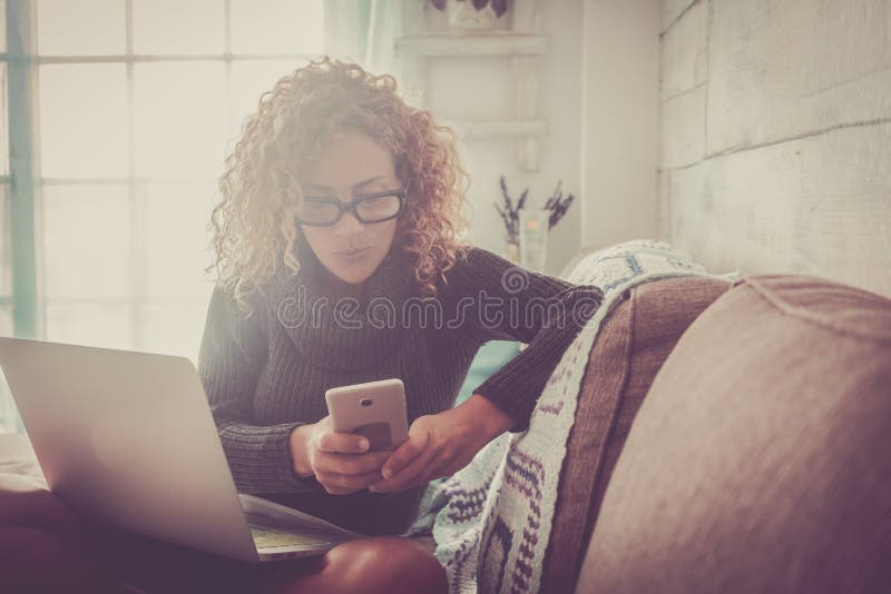 Freelance people at work at home - beautiful adult caucasian woman sit on the sofa with phone device and laptop computer working -