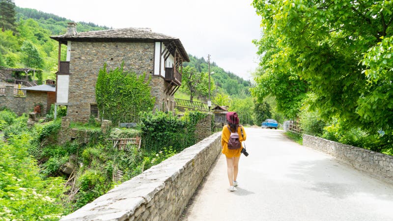 Freelancer photographer walking holding camera from behind visit on a solo tour a typical village in the balkans. Caucasian woman