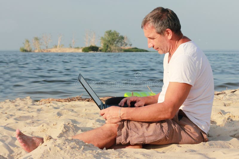 Muž dizajnér pracuje on-line na opustený ostrov, na pláži.