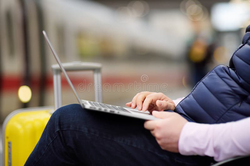 Freelancer working with a laptop in a train station while is waiting for transport.