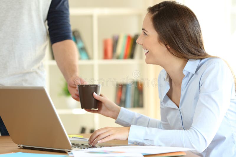 Happy freelancer working at home and her husband giving a cup of coffee. Happy freelancer working at home and her husband giving a cup of coffee