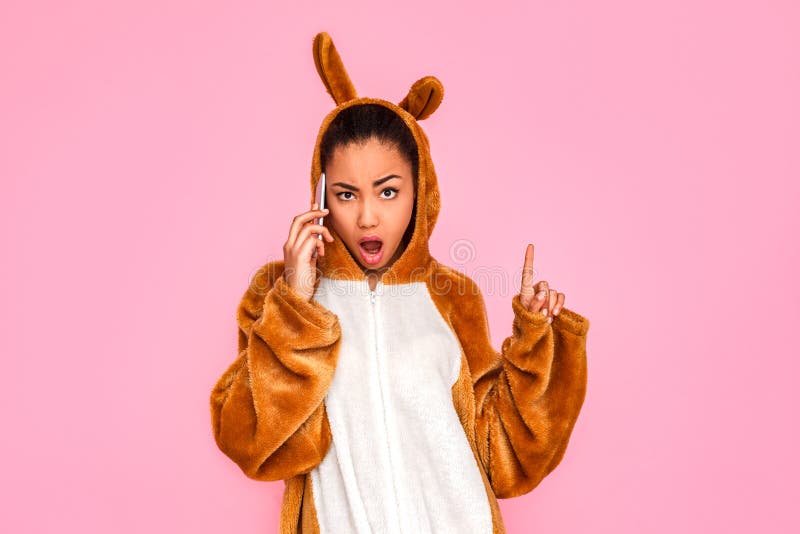 freestyle Mujer joven en la situación del kigurumi en hablar rosado en el teléfono que mira la cámara descarada foto de archivo freestyle Mujer joven en la situación del kigurumi en hablar rosado en el teléfono que mira la cámara descarada foto de archivo