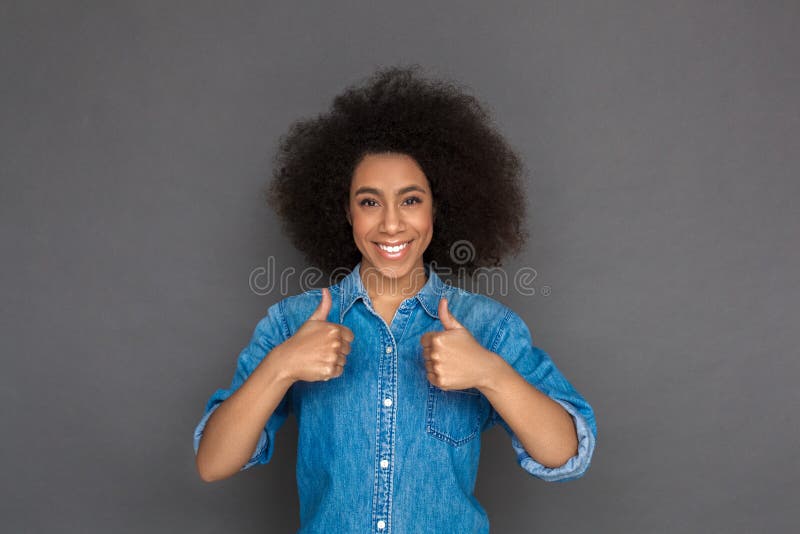 Young mixed race woman standing isolated on grey wall showing thumbs up with two hands looking camera smiling cheerful. Young mixed race woman standing isolated on grey wall showing thumbs up with two hands looking camera smiling cheerful