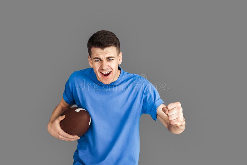 Mladý muž stojící na šedá držení ragby koule ječivé na motivované podporující oblíbený tým.