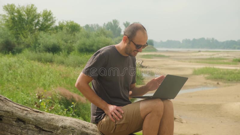 Freiberufler bei einer Online-Konferenz vor dem Hintergrund eines Waldes und eines Flusses.