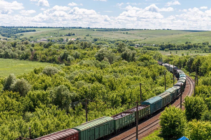 The Freight Railroad Train Rides through Fields and Hills Amidst Green