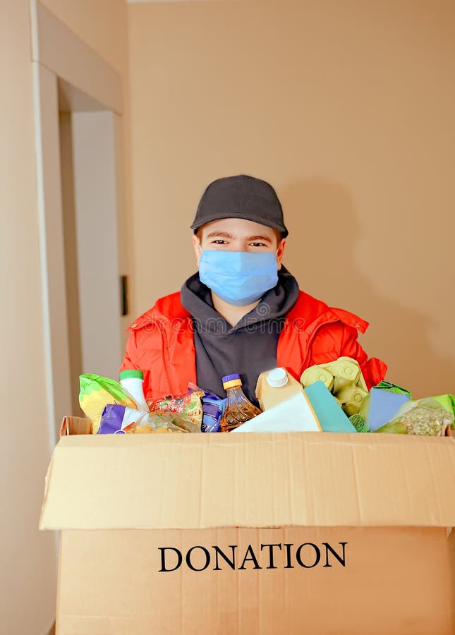 Freiwilliger junger Kaukasier in einer medizinischen Schutzmaske und Handschuhe mit einer Spenderbox mit Nahrung Nahaufnahme Haus lizenzfreies stockfoto Freiwilliger junger Kaukasier in einer medizinischen Schutzmaske und Handschuhe mit einer Spenderbox mit Nahrung Nahaufnahme Haus lizenzfreies stockfoto