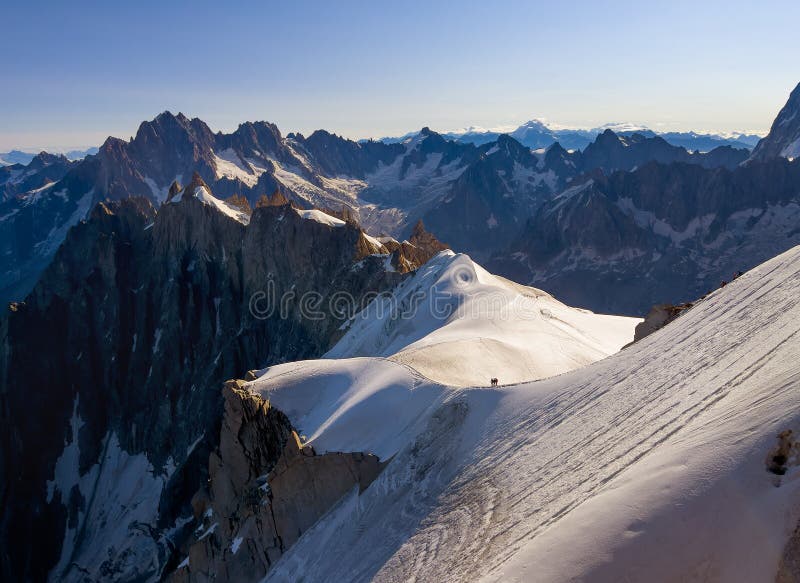 French Alps mountains peaks panorama view with silhouettes of climbers as roping team descending on the snowy slope under Aiguille du Midi 3842m. Beauty of Nature and extreme people activity concept