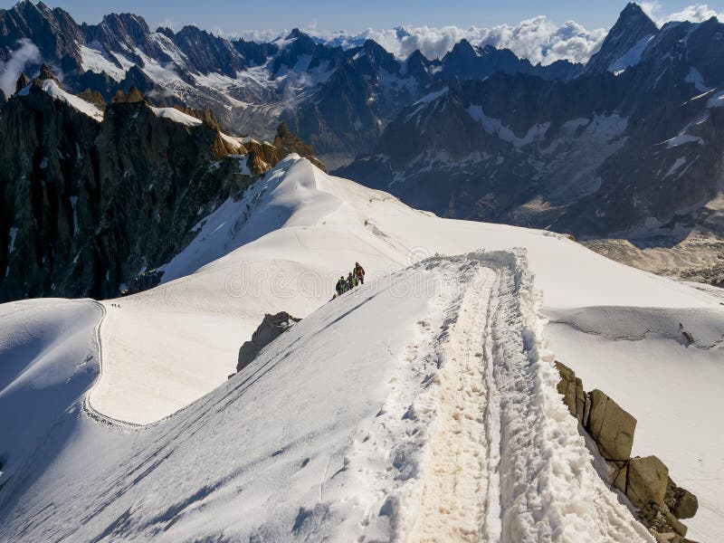 French Alps mountains snowy ridge view with silhouettes of climbers as roping team descending on the snowy slope under Aiguille du Midi 3842m. The beauty of Nature and extreme people activity concept