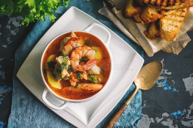 French fish soup Bouillabaisse with seafood, salmon fillet, shrimp, rich flavor, delicious dinner in a white beautiful plate. Close up.