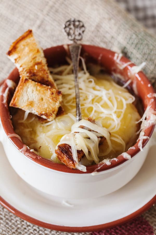 French Onion Gratin Soup in a Clay Pot, Authentic Recipe, Wooden Spoon on a Cutting Board on an