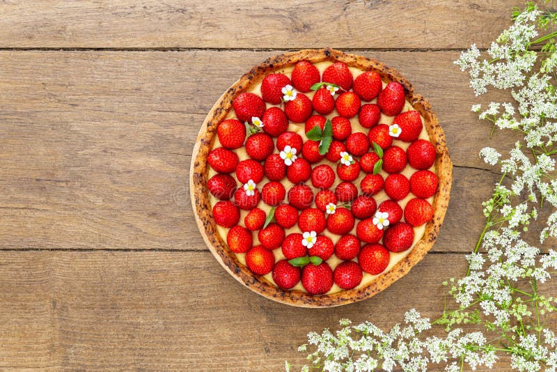 French strawberry tart spread with wild strawberry leaves and flowers circled by white flower on oak wood background. Flat Lay, royalty free stock photos French strawberry tart spread with wild strawberry leaves and flowers circled by white flower on oak wood background. Flat Lay, royalty free stock photos