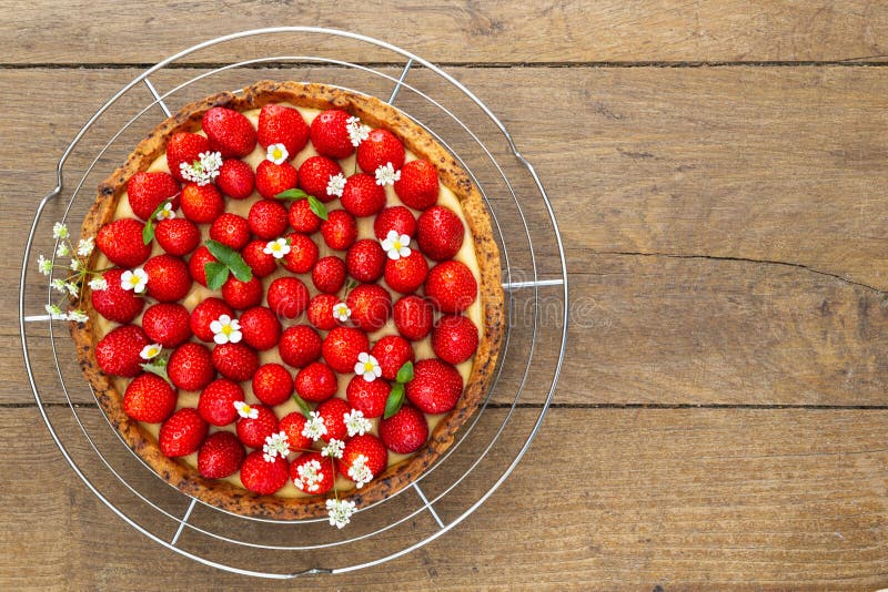 French strawberry tart spread with wild strawberry leaves and flowers on a stainless cooling rack on a oakwood background. Flat la stock photo French strawberry tart spread with wild strawberry leaves and flowers on a stainless cooling rack on a oakwood background. Flat la stock photo