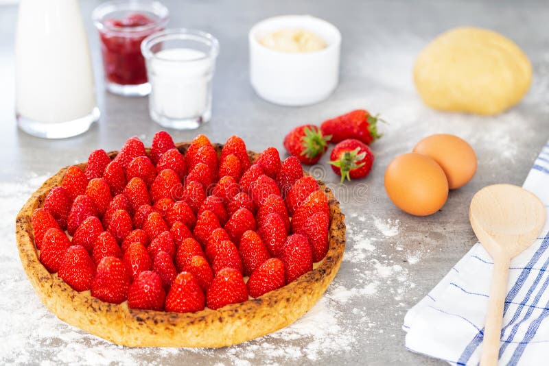 French strawberry tart with sugar, dough, spoon and eggs on a grey background with flour royalty free stock photo French strawberry tart with sugar, dough, spoon and eggs on a grey background with flour royalty free stock photo