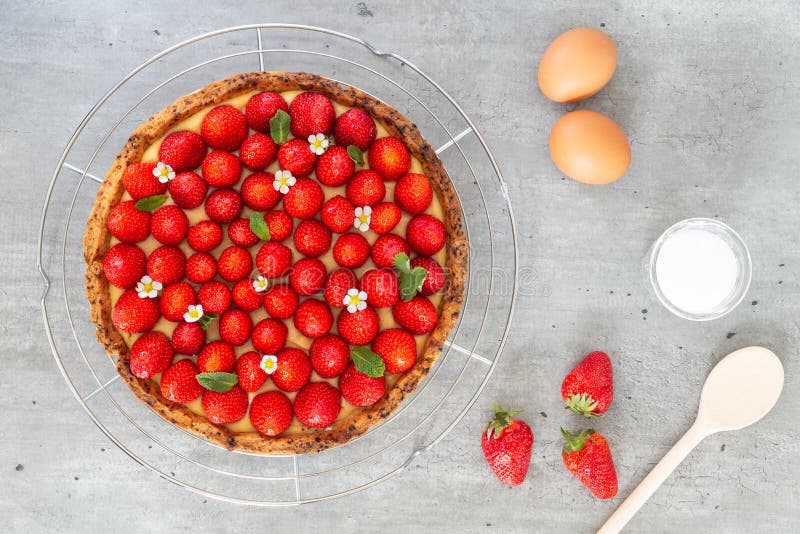 French strawberry tart with wild strawberry leaves and flowers on top of a cooling rack with eggs, sugar and spoon stock images French strawberry tart with wild strawberry leaves and flowers on top of a cooling rack with eggs, sugar and spoon stock images