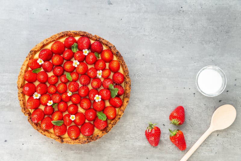 French strawberry tart with wild strawberry leaves and flowers on top of a cooling rack with sugar and spoon on a grey background stock image French strawberry tart with wild strawberry leaves and flowers on top of a cooling rack with sugar and spoon on a grey background stock image