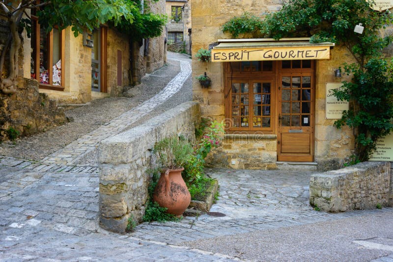 Beynac-et-Cazenac, France â€“ August 25, 2015: Typical French townscape with a gourmet store front and cobblestone streets in the traditional town Beynac-et-Cazenac along Dordogne river in Perigord region, France. Beynac-et-Cazenac, France â€“ August 25, 2015: Typical French townscape with a gourmet store front and cobblestone streets in the traditional town Beynac-et-Cazenac along Dordogne river in Perigord region, France.