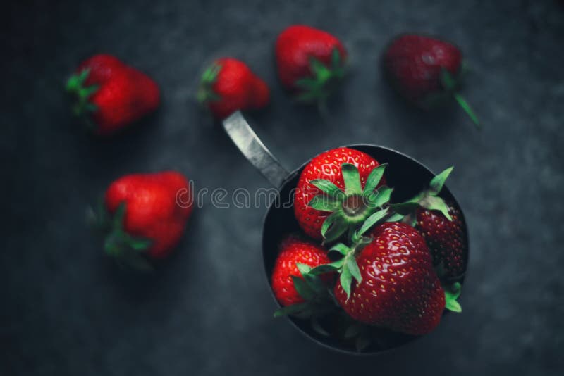 Fresas maduras dispersadas alrededor de una taza del hierro Foto oscura imágenes de archivo libres de regalías Fresas maduras dispersadas alrededor de una taza del hierro Foto oscura imágenes de archivo libres de regalías