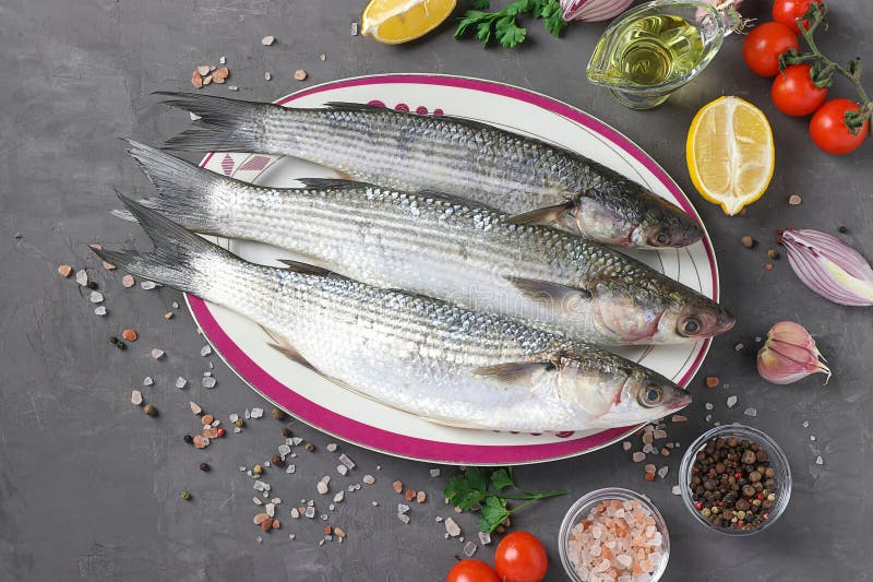 Frescos listos para cocinar mullets crudos con ingredientes y aderezos como los tomates de limón perejil cebolla roja y. Fresco listo para cocinar mulas crudas con ingredientes y condimentos como los tomates de limón perejil cebolla roja y aceite de oliva en la vista superior gris