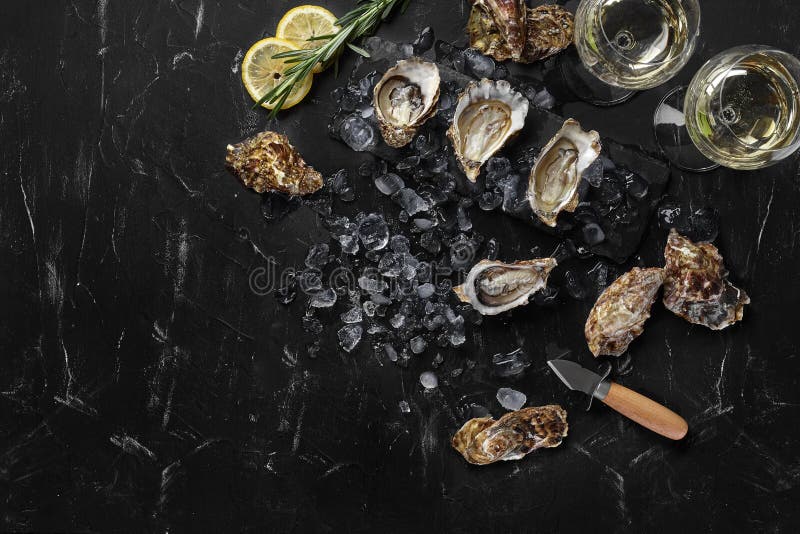 Fresh opened oysters, ice, lemon on a rectangle slate and champagne are on a black stone textured background. Top view