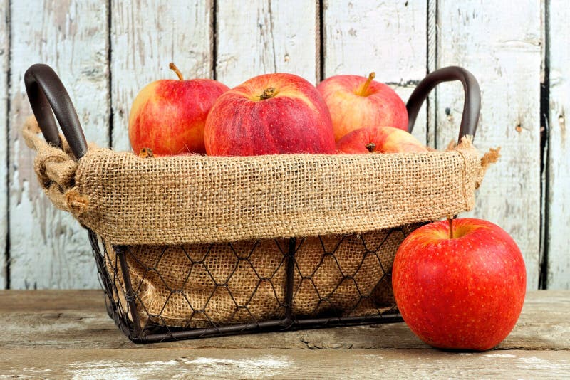 Fresh apples in vintage wire basket against white wood
