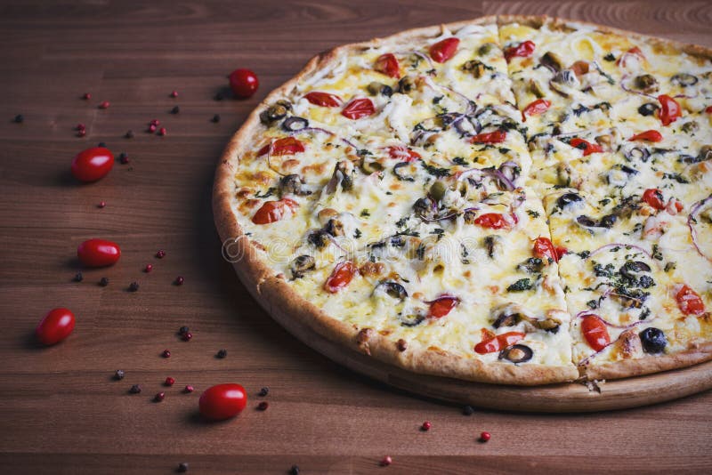 The fresh baked pizza with olives and tomatoes on the wooden background