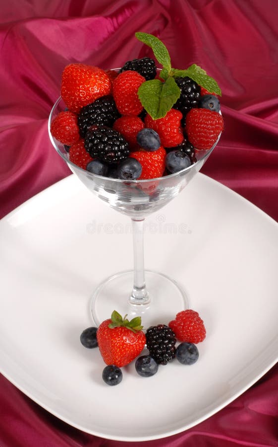 Fresh berries topped with mint in and around a martini glass