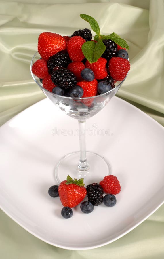 Fresh berries topped with mint in and around a martini glass res