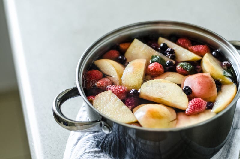 Fresh boiled apple kompot with blueberries and blackberries, in pot on kitchen towel, fresh fruit drink, summer beverage