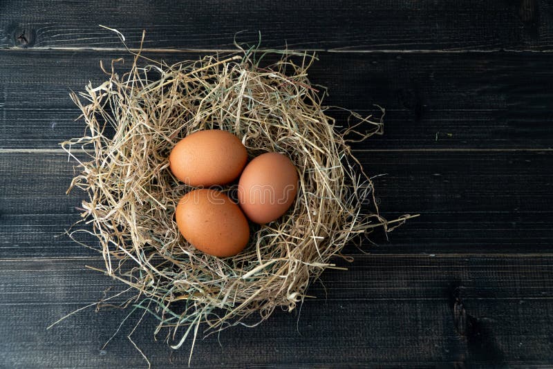 Fresh brown chicken eggs in hay nest on black wooden background. 