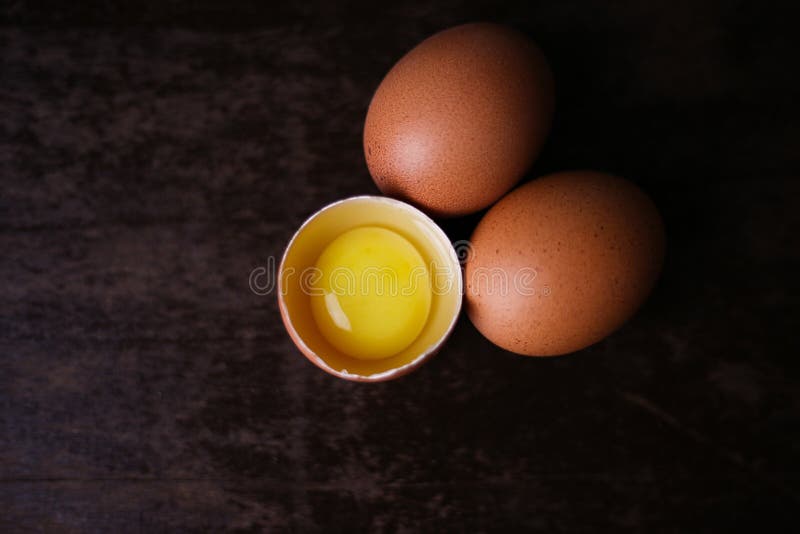 Fresh Brown Eggs and a Broken Egg with Yolk on a Dark Wooden Background