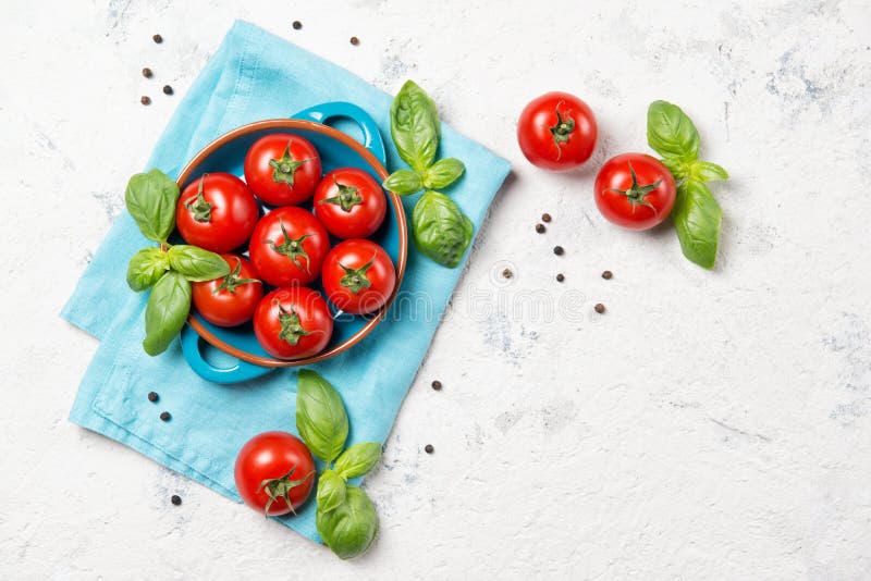 Fresh cherry tomatoes in a bowl, basil leaves and black pepper on stone table, closeup, top view with copy space