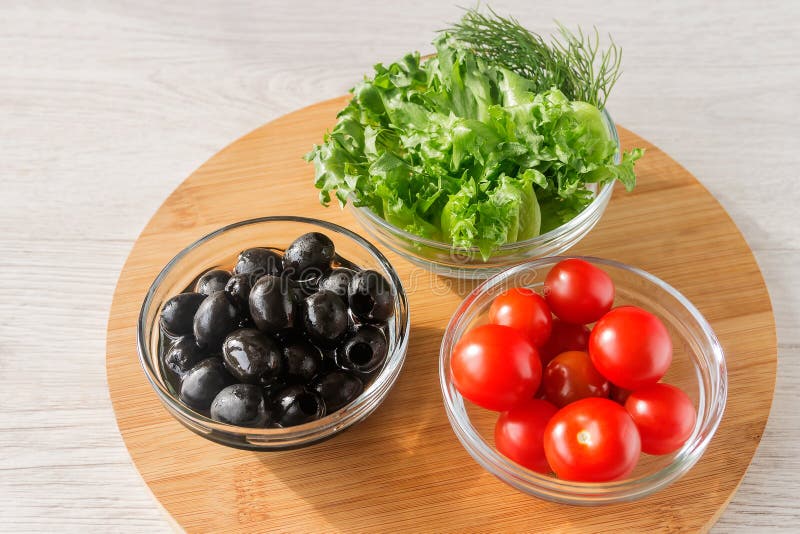 On a wooden kitchen board, three glass bowls with cherry tomatoes, olives, lettuce for a snack. On a wooden kitchen board, three glass bowls with cherry tomatoes, olives, lettuce for a snack.