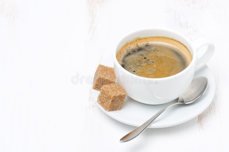 Fresh coffee with sugar cubes on a white wooden table