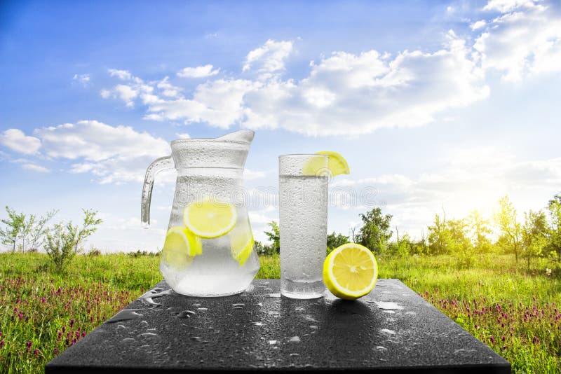 Fresh cold water with lemon and ice in a pitcher on the table.Homemade lemonade with fresh citruses on the background of nature. Quenching thirst.The royalty free stock image Fresh cold water with lemon and ice in a pitcher on the table.Homemade lemonade with fresh citruses on the background of nature. Quenching thirst.The royalty free stock image