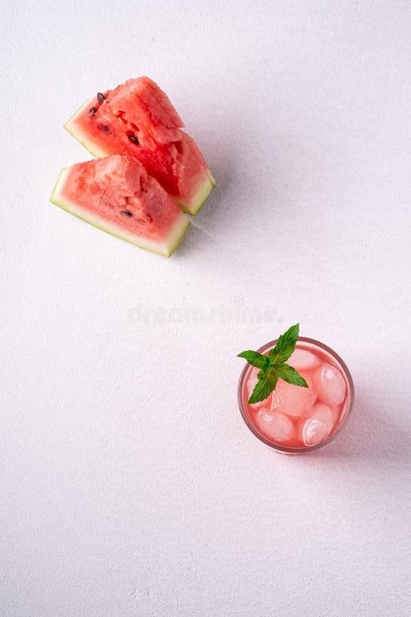 Fresh cold watermelon juice with ice cubes and green mint leaf in glass drink close to two slices of watermelon, top view