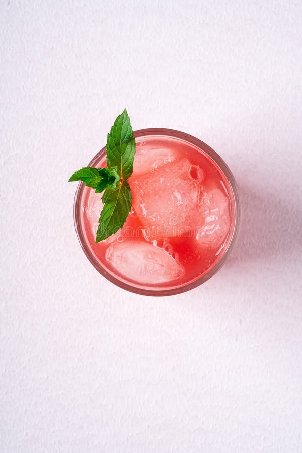 Fresh cold watermelon juice with ice cubes and green mint leaf in glass drink on white background, top view