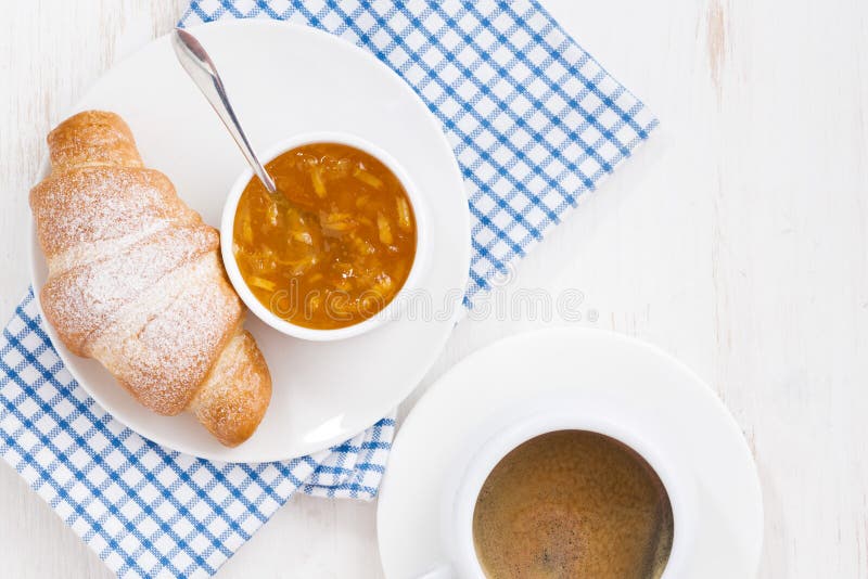 Fresh croissant with orange jam and coffee, top view