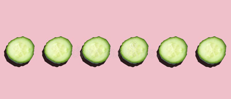Fresh cucumber slices in a row on a pink background with hard light.