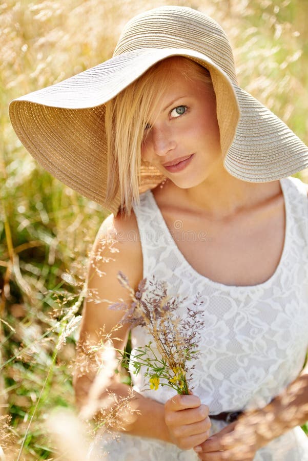 Fresh-faced country beauty. Gorgeous young beauty picking wildflowers in a field while wearing a straw hat.