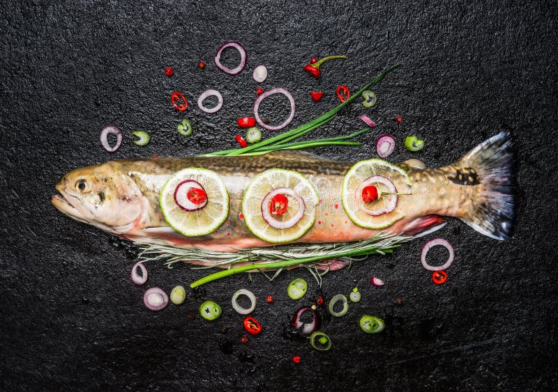 Fresh fish with delicious chopped seasoning ready for tasty cooking on dark background, top view