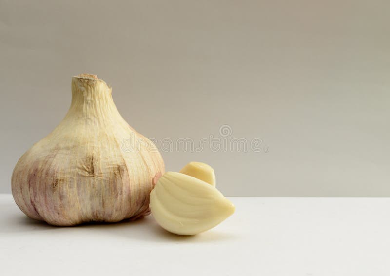 Fresh Garlic Head Next To Two Peeled Garlic Cloves on White Background