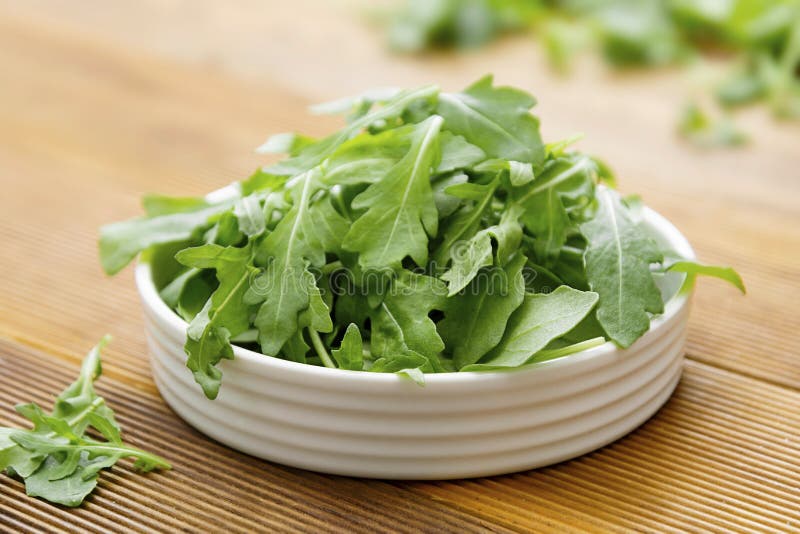 Fresh green rocket salad in white round plate. Healthy salad isolated on wooden table. Copy space