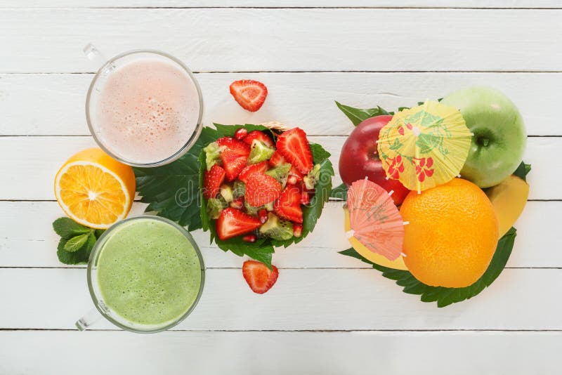 Fresh green smoothies and a milkshake of strawberries in glass glasses with tropical fruits on white boards stock image Fresh green smoothies and a milkshake of strawberries in glass glasses with tropical fruits on white boards stock image