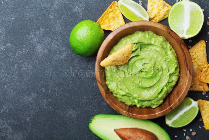 Fresh guacamole dip with avocado, lime and nachos on black table top view. Copy space.Traditional mexican food.