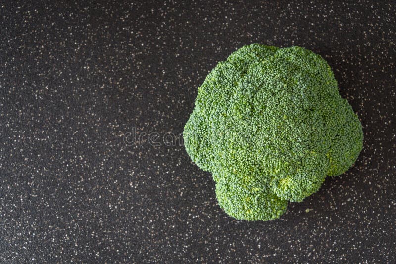 Fresh Head of Broccoli Ready for Cutting Up on a Large Black Cutting