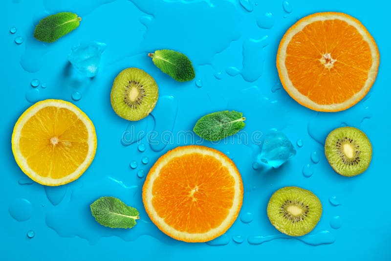 Fresh juicy slices of orange, kiwi fruit, lemon and mint leaves on bright blue background covered with water drops